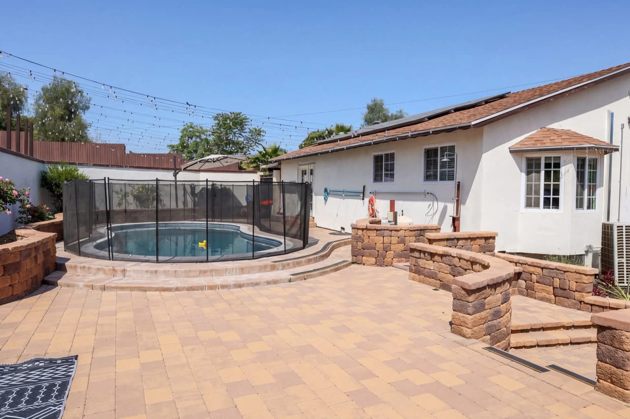 Richards fenced pool beside a paved patio and stone seating wall