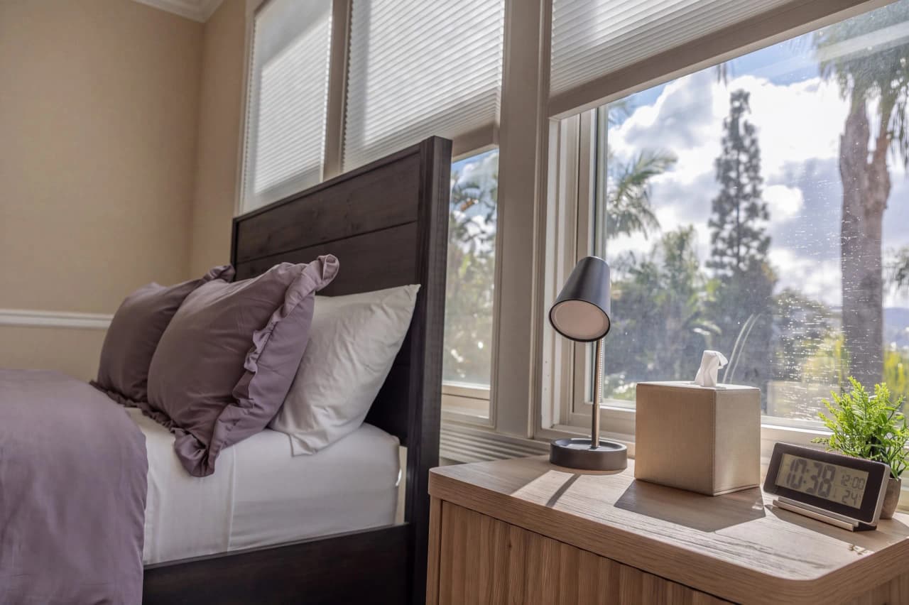 Made bed and nightstand with a lamp beside a Shasta bedroom window