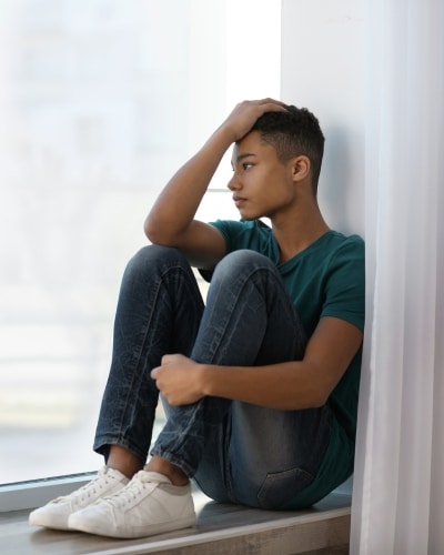 Upset teenage boy sitting alone near window