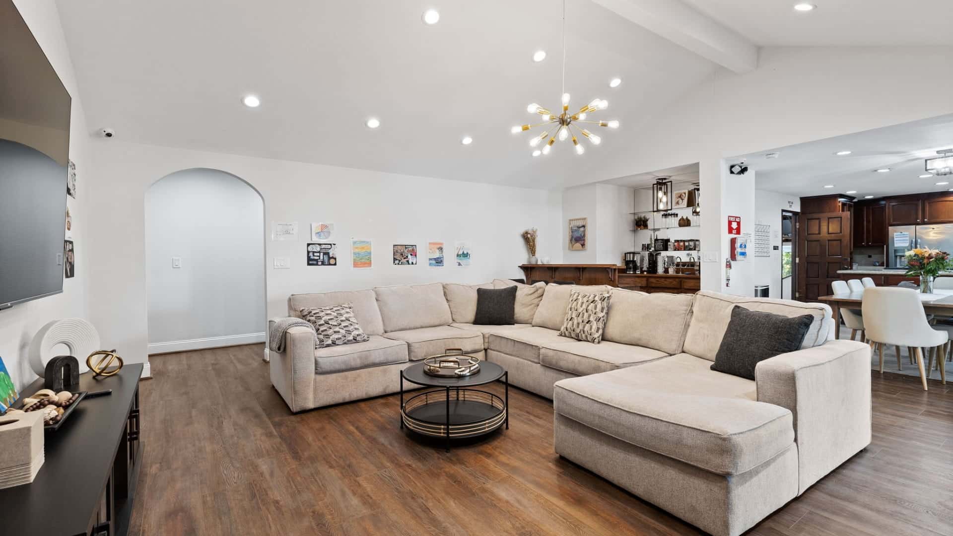 Bright living room with large sectional sofa, modern lighting, and open concept design. Home interior with hardwood floors.