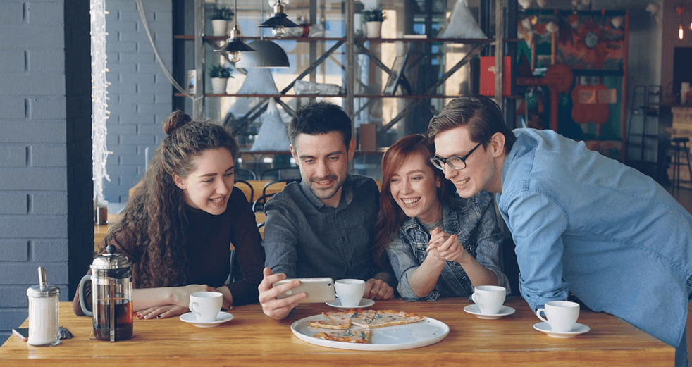 Teen mental health: Friends enjoy pizza and phone at cafe. Support and connection for teen mental wellness.
